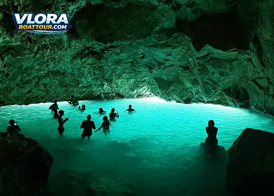 Visitors swimming inside the Blue Cave near Vlore, surrounded by glowing turquoise water and dramatic limestone walls illuminated by natural light filtering through the cave entrance.